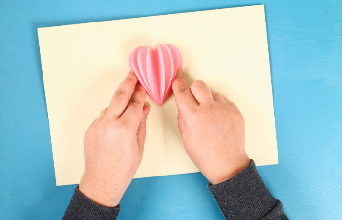 DIY Valentine's Day Cards for Kids gluing a fan of hearts to the fold of a card to create a pop up card.
