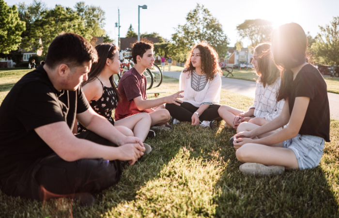 teens sitting around in a circle on the grass.l