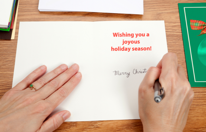 writing inside a card that says wishing you a joyous holiday season.