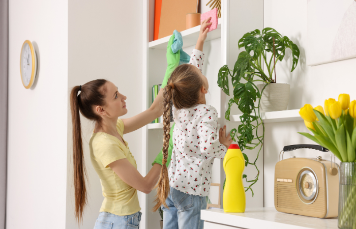 mom and daughter doing some dusting on a shelf.