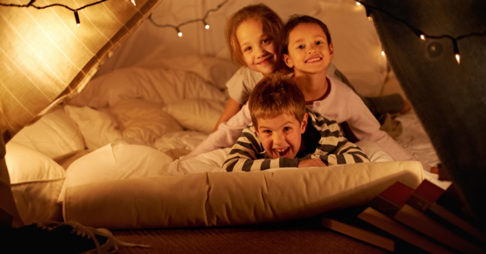 3 kids in a fort made out of blankets and fairy lights