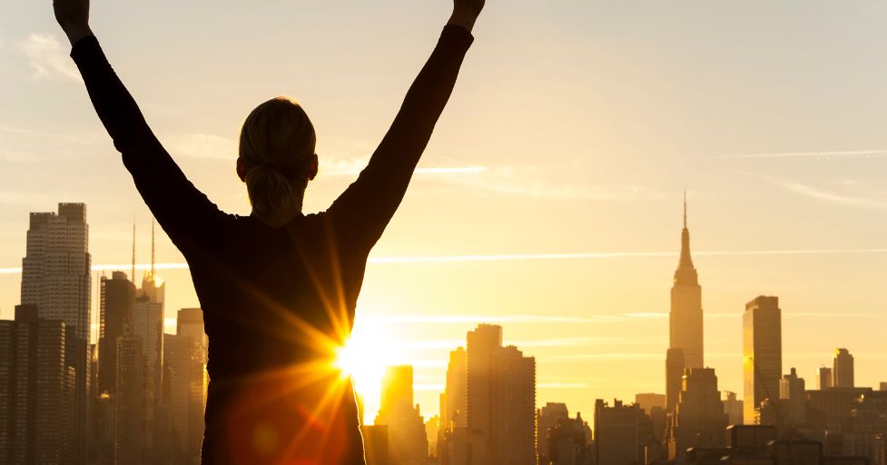 woman holding up arms triumphantly with a city landscape in the background