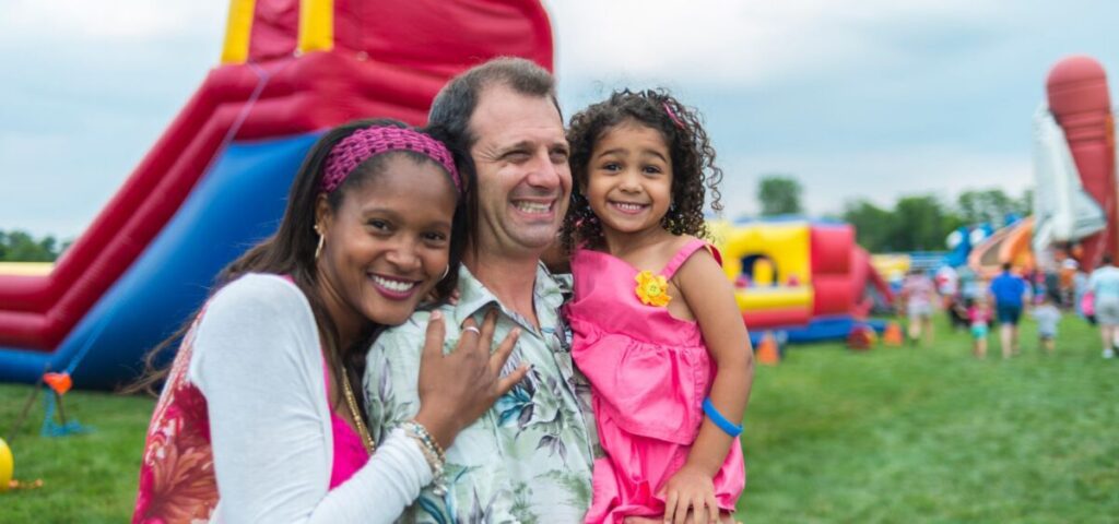 mom and dad and daughter at a fair with bounce houses