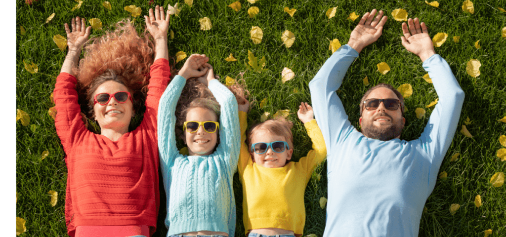 family laying on grass with arms up wearing sun glasses