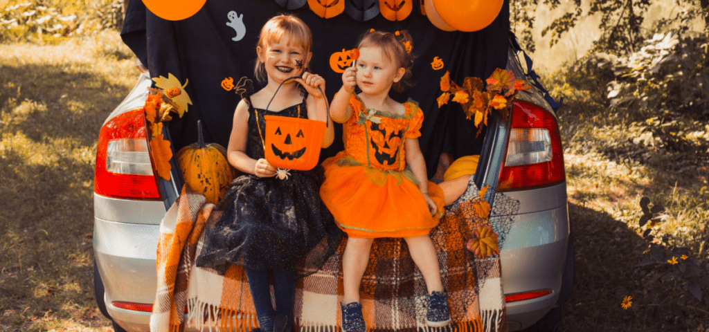 two girls sitting on the back of a car with halloween decorations for a trunk or treat