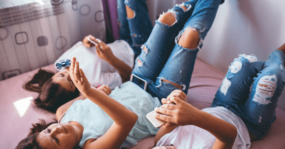 three teen girls laying on a bed looking at their phone social media impact on teen relationships